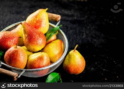 Fresh pears with leaves in a colander. On a black background. High quality photo. Fresh pears with leaves in a colander.