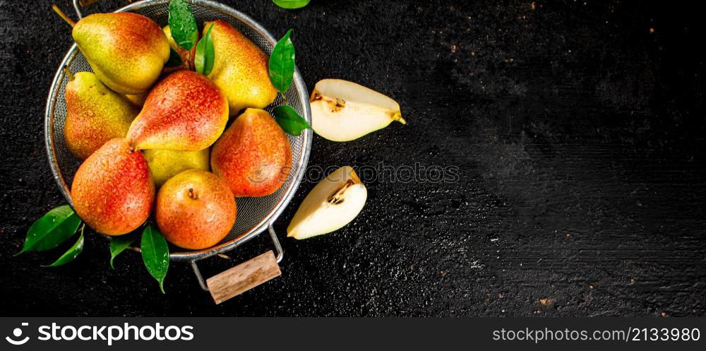 Fresh pears with leaves in a colander. On a black background. High quality photo. Fresh pears with leaves in a colander.