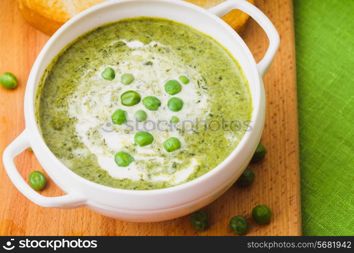 Fresh peas cream soup in a bowl on a wooden board and croutons