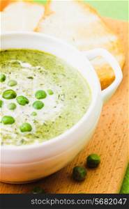 Fresh peas cream soup in a bowl on a wooden board and croutons