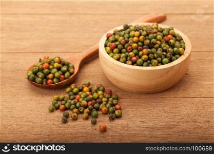 fresh peppercorns in wooden bowl and spoon on wood background