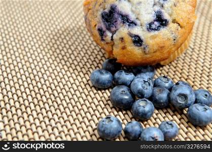 Fresh picked blueberries next to a berry muffin on a woven wood place mat. Blueberries And Muffin