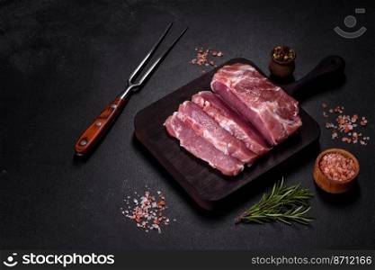 Fresh piece of raw pork with spices, salt and herbs on a wooden cutting board. Cooking grilled meals at home. Fresh piece of raw pork with spices, salt and herbs on a wooden cutting board