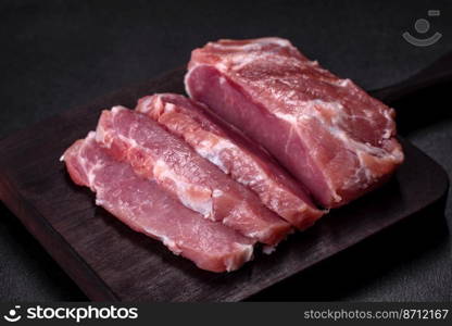 Fresh piece of raw pork with spices, salt and herbs on a wooden cutting board. Cooking grilled meals at home. Fresh piece of raw pork with spices, salt and herbs on a wooden cutting board