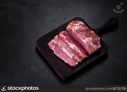 Fresh piece of raw pork with spices, salt and herbs on a wooden cutting board. Cooking grilled meals at home. Fresh piece of raw pork with spices, salt and herbs on a wooden cutting board