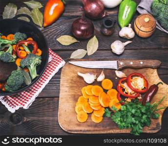 fresh pieces of broccoli, carrots and red peppers in a black cast-iron frying pan on a brown table, top view
