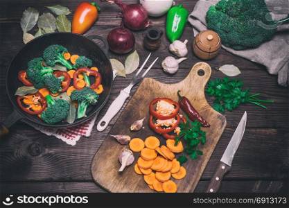 fresh pieces of carrots, broccoli and red pepper on a wooden kitchen board, next to a round cast-iron frying pan