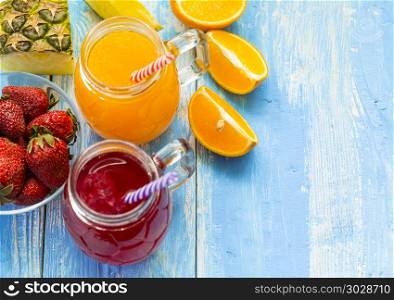 Fresh pineapple and strawberry smoothie in glasses with fruits on a blue wooden rustic background. Freshly blended summer drink nice to drink during a hot day.. Fresh pineapple and strawberry smoothie in glasses with fruits o