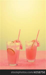 fresh pink alcoholic cocktail with grapefruit lemon slice ice cubes against yellow background