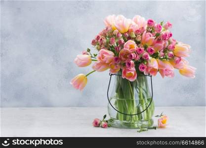 fresh pink and yellow tulips and roses in glass vase on gray background. Pink and yellow tulips and roses