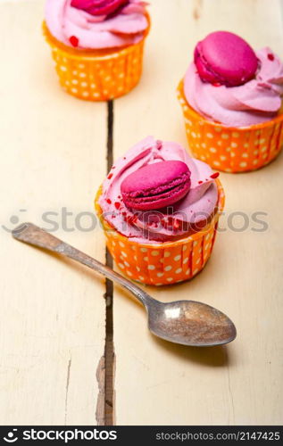 fresh pink berry cream cupcake with macaroon on top over rustic wood table