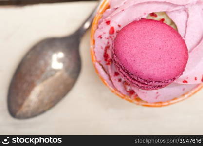 fresh pink berry cream cupcake with macaroon on top over rustic wood table