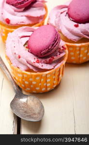 fresh pink berry cream cupcake with macaroon on top over rustic wood table