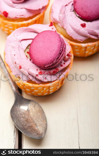 fresh pink berry cream cupcake with macaroon on top over rustic wood table