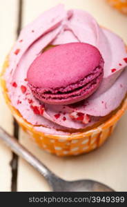 fresh pink berry cream cupcake with macaroon on top over rustic wood table