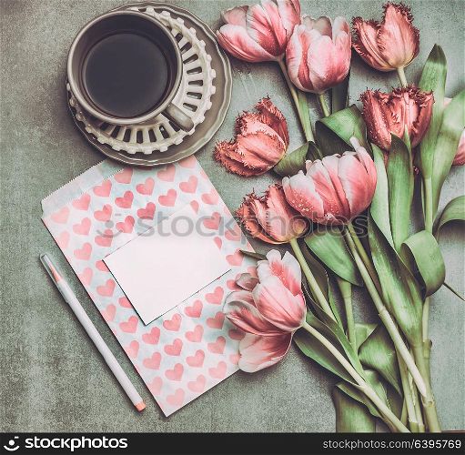 Fresh pink pale tulips flowers with heart letter , blank paper , marker and cup of coffee , top view. Nostalgic Mother day greeting card or spring holidays mock up
