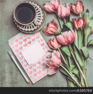 Fresh pink pale tulips flowers with heart letter , blank paper , marker and cup of coffee , top view. Nostalgic Mother day greeting card or spring holidays mock up