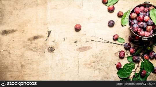 Fresh plums with green leaves. On wooden background.. Fresh plums with green leaves.