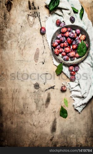 Fresh plums with green leaves. On wooden background.. Fresh plums with green leaves.