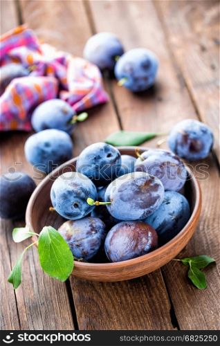 Fresh plums with green leaves on wooden rustic background