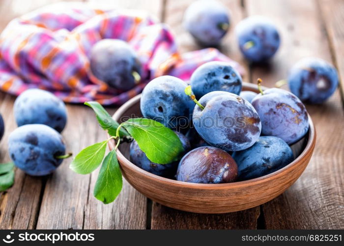 Fresh plums with green leaves on wooden rustic background