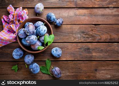 Fresh plums with green leaves on wooden rustic background, top view