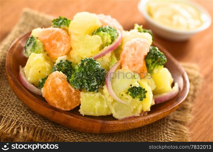 Fresh potato, broccoli, mandarin and onion salad with mayonnaise on wooden plate (Selective Focus, Focus on the mandarin and the broccoli in the front)
