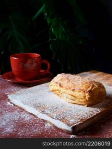 Fresh Puff on the table with a red cup of coffee on the black background.. Puff pastry dessert red cup coffee black background