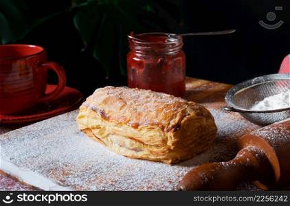 Fresh Puff staffed with plum or red currant jam on the table with a red cup and jar of jam on the black background.. Puff pastry dessert red jam viburnum cherry cup coffee black background