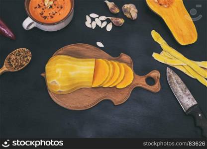 fresh pumpkin on a wooden kitchen board and cream on a pumpkin soup on a black background, top view