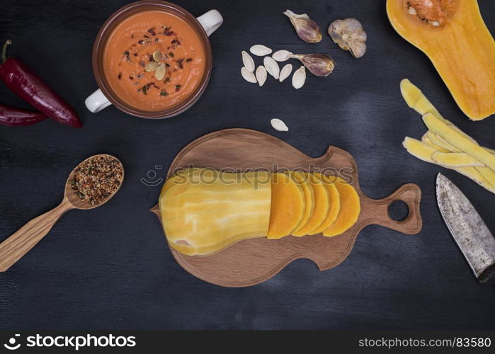 fresh pumpkin sliced into pieces on a wooden kitchen board and ingredients for cooking cream soup on a black background, top view