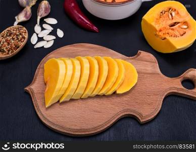 fresh pumpkin sliced into pieces on a wooden kitchen board for cooking on a black wooden background, top view