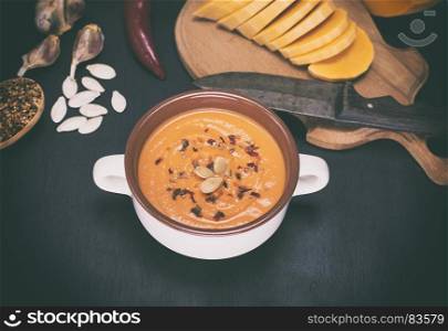 fresh pumpkin soup in a ceramic plate, on a black wooden table