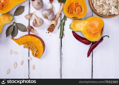 fresh pumpkin with seeds, garlic and spices on a white wooden background, empty space at the bottom