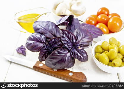 Fresh purple basil in a mortar, olives, tomatoes and ch&ignons in bowls, vegetable oil in gravy boat and a knife on white wooden board background