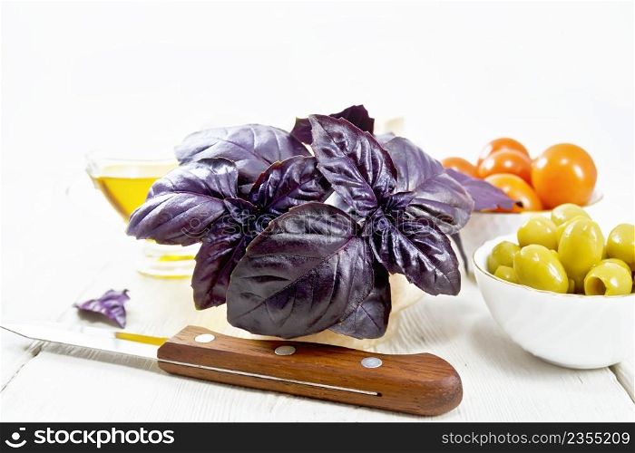 Fresh purple basil in a mortar, olives, tomatoes and champignons in bowls, vegetable oil in gravy boat and a knife on wooden board background