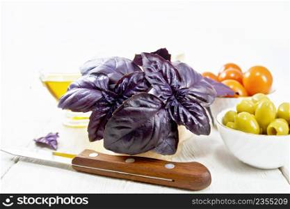 Fresh purple basil in a mortar, olives, tomatoes and champignons in bowls, vegetable oil in gravy boat and a knife on wooden board background