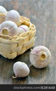 Fresh purple garlic in a small straw basket on old wooden table