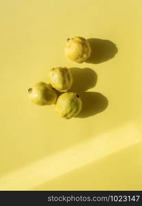 Fresh quince fruits on yellow paper background. Above view of four quinces in natural light. Isolated fall yellow fruits. Minimal image.