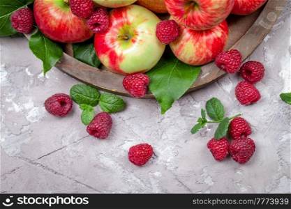Fresh raspberries and apples on old wooden plate on a concrete background. Healthy concept. Natural healthy food. Organic food.