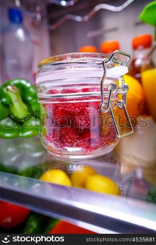 Fresh raspberries in a glass jar on a shelf open refrigerator. Healthy food.