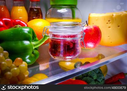 Fresh raspberries in a glass jar on a shelf open refrigerator. Healthy food.