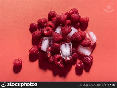 Fresh raspberries in a pile with ice cubes on a red background in sunlight. Above view of tasty summer fruits. Ingredients for berries lemonade.