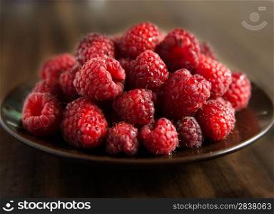 Fresh raspberries on brown plate, dark background, selective focus