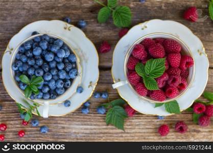 fresh raspberry and blueberry with green leaves in cups, top view