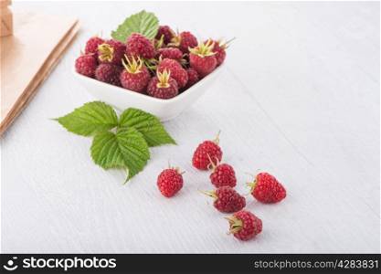 Fresh raspberry in a white bowl on wooden table.