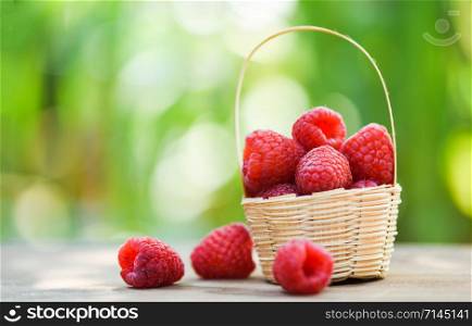 Fresh raspberry in basket / Close up red ripe raspberries fruit on wooden and nature green blur background