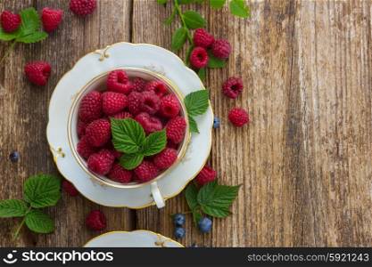 fresh raspberry in cup with green leaves on wooden background, top view
