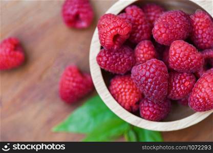 Fresh raspberry in wooden bowl / Close up red raspberries fruit and green leaf top view
