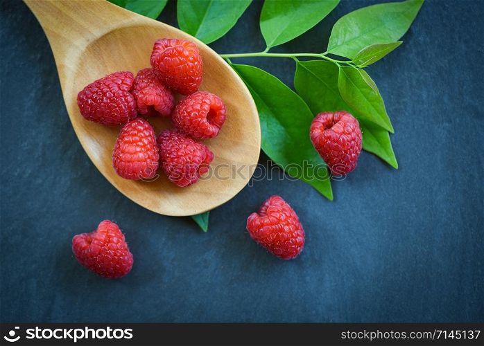Fresh raspberry on wooden spoon / Top view red ripe raspberries fruit and green leaf on dark background